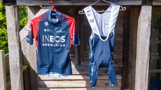 BioRacer INEOS Grenadiers kit hangs on coat hangers in front of a wooden shed
