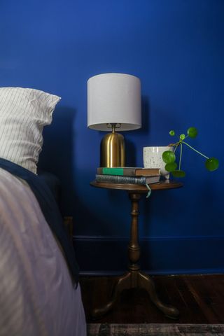 A bedroom with dark blue walls, a nightstand, and a brass lamp