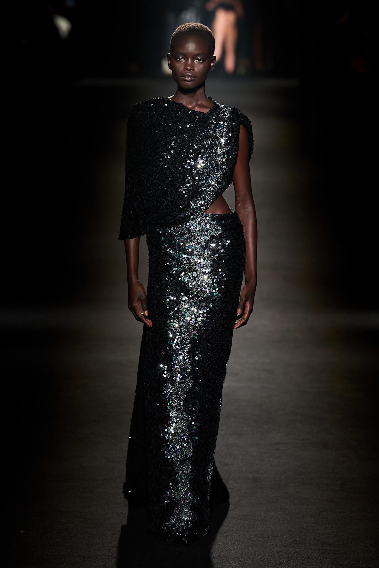 A model walking in the F/W 26 Balenciaga show wearing a black sequin gown with cutouts.