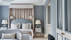 Bedroom with pale blue walls, a floral canopy and pale blue headboard, neutral bedding, white vintage nightstands, and a small blue loveseat