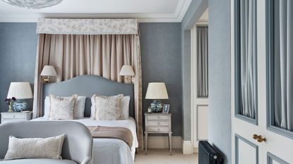 Bedroom with pale blue walls, a floral canopy and pale blue headboard, neutral bedding, white vintage nightstands, and a small blue loveseat