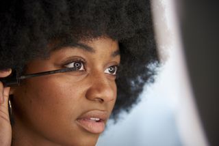 Close-up view of an Afro woman applying mascara on her eyelashes while doing her makeup. Concept of cosmetics, makeup and beauty.