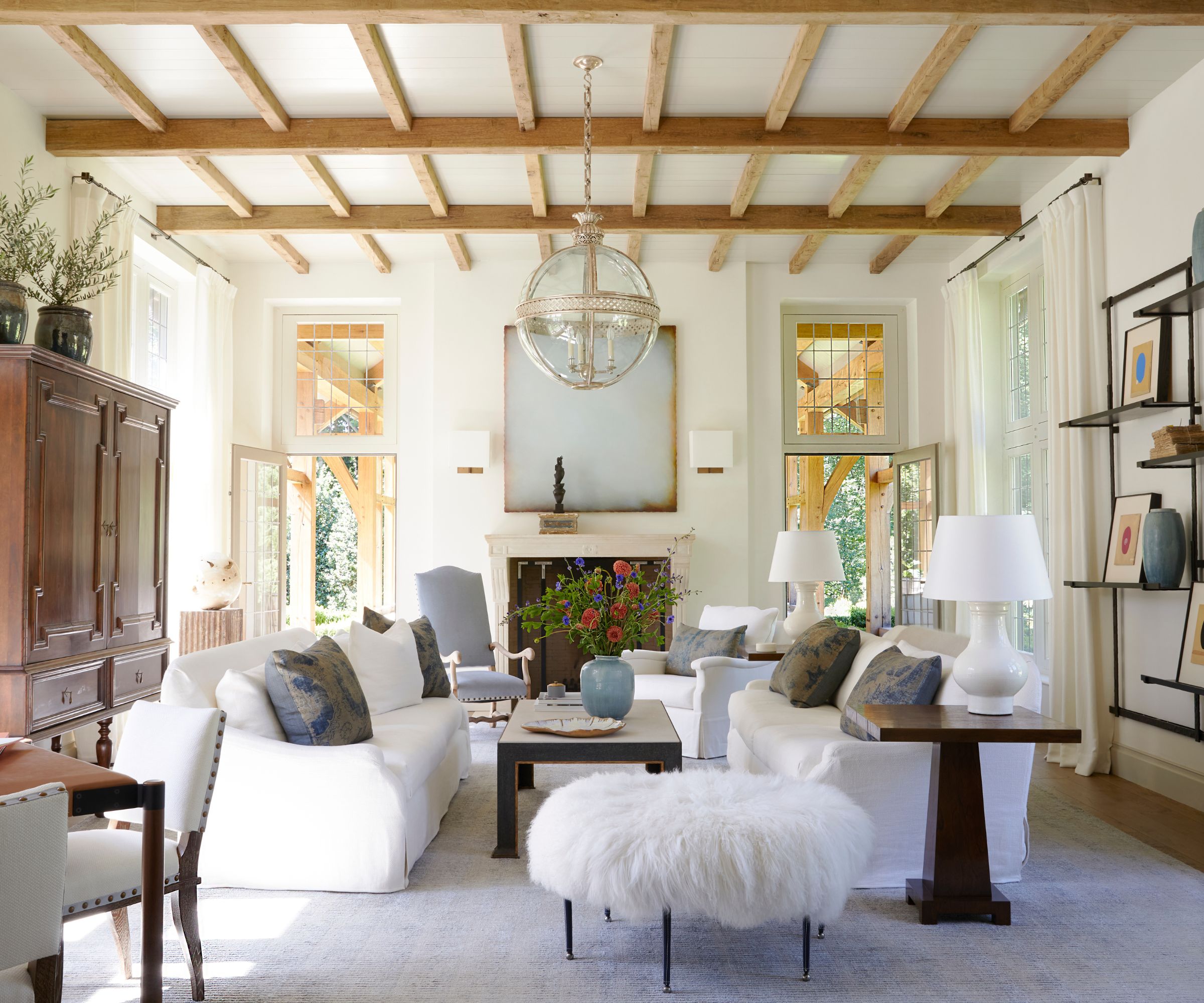 Living room with beams, white walls, white sofas and fluffy stool and large low glass pendant