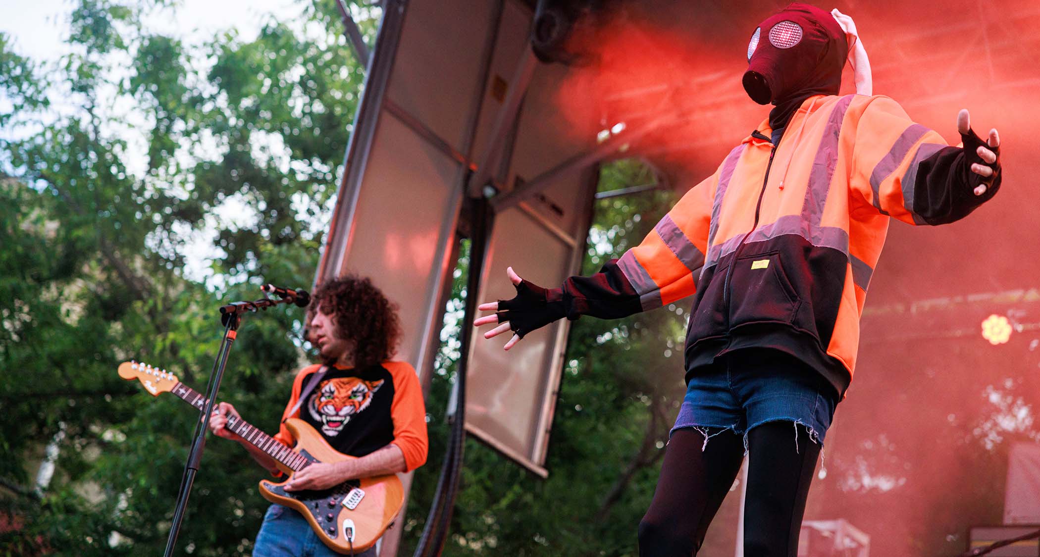 Ethan Ives of Car Seat Headrest plays an orange Strat as vocalist Will Toledo wears hi-viz and a gas mask