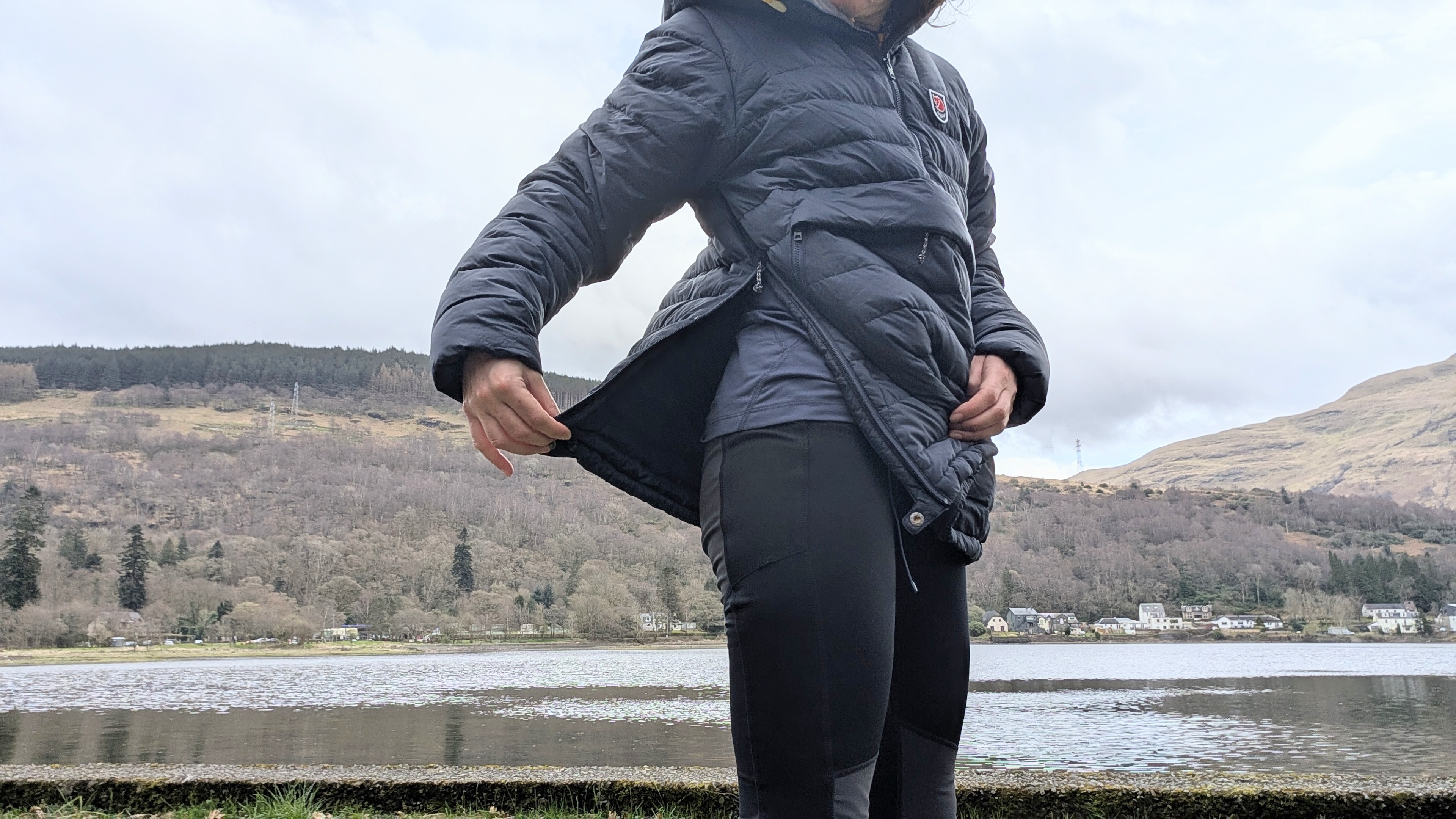 A woman shows the side zip on a blue Fjallraven Expedition Pack Down Anorak