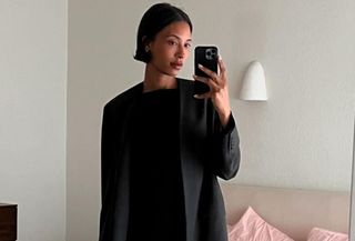 Woman wears black blazer and black mini dress while taking mirror selfie.