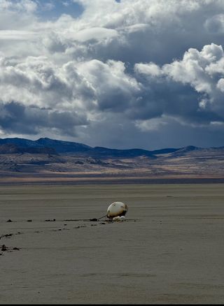 a cone-shaped capsule lies on the desert floor under cloudy skies