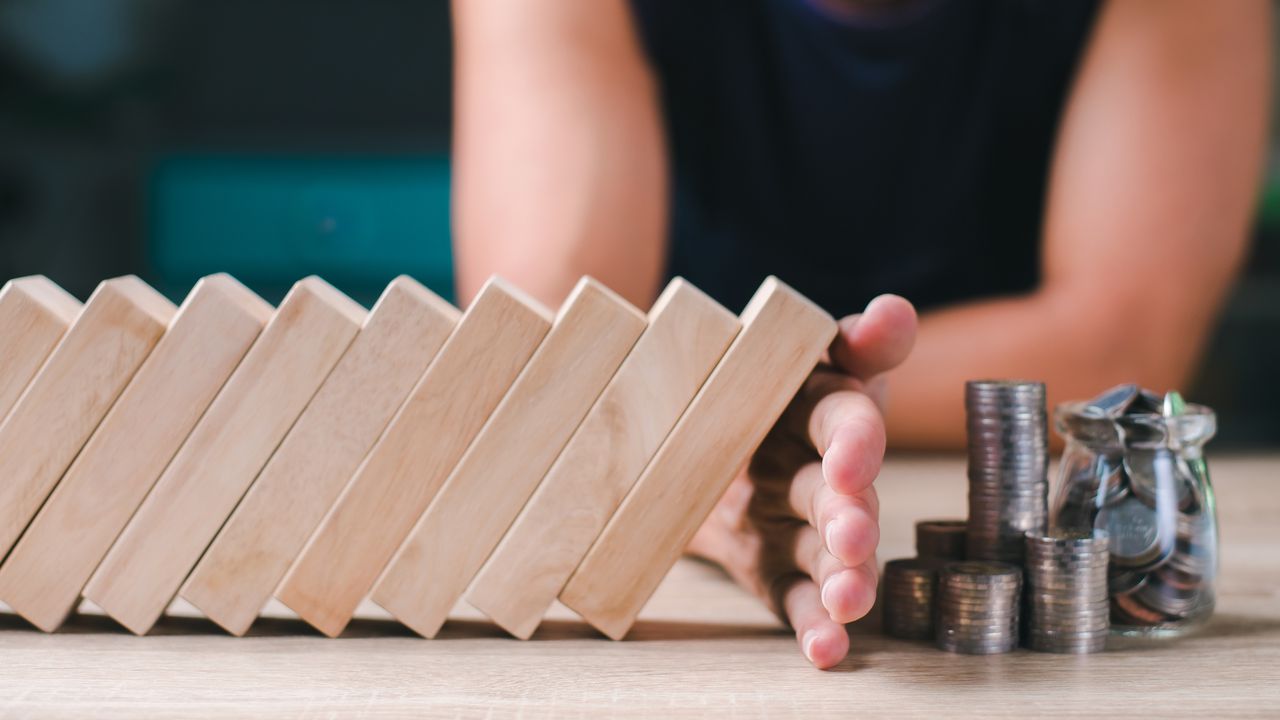 A woman puts her hand protectively between tipping wooden blocks and stacks of coins.