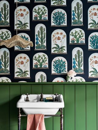 A powder room with green wall panels behind a white sink and below botanical wallpaper