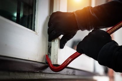 dangerous masked burglar with crowbar breaking into a victim's home door,concept