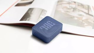 JBL Go Essential bluetooth speaker on a white background, leaning on a book
