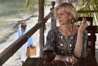 Francesca Bower (Siobhan Redmond) sits at a table alone at Catherine's bar, in the outdoor area covered with a canopy. There is an empty glass on the table in front of her, and she looks deep in thought.