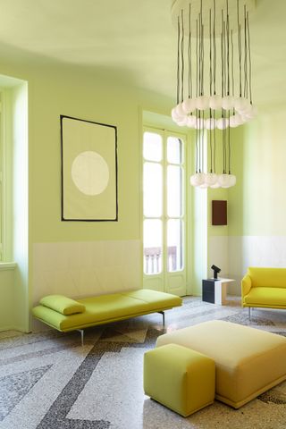 A color-drenched neon yellow sitting room. The walls are neon yellow as well as the doors, artwork, lounge chaise, and ottomans.