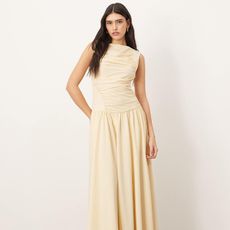 model wears butter yellow drop waist dress with ruching and draping from ASOS ARRANGE collection while posing