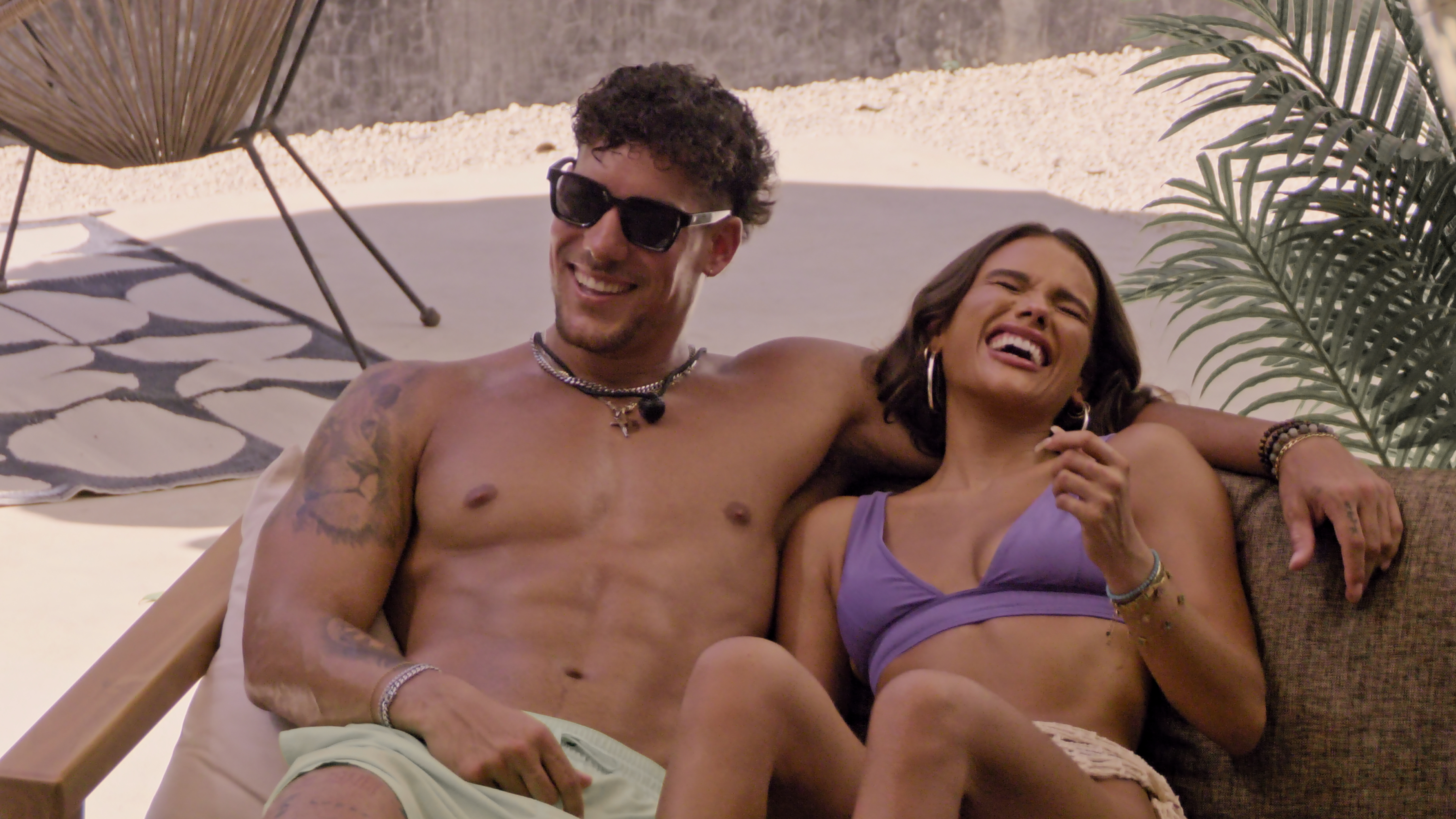daniel and lucy sit on a lounge chair together laughing in perfect match