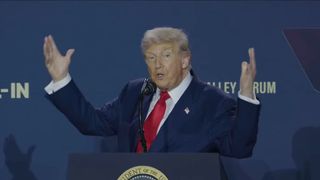 A still from a livestream of US President Donald Trump speaking at an AI summit in Washington DC, gesticulating with his hands at the name "artificial intelligence"