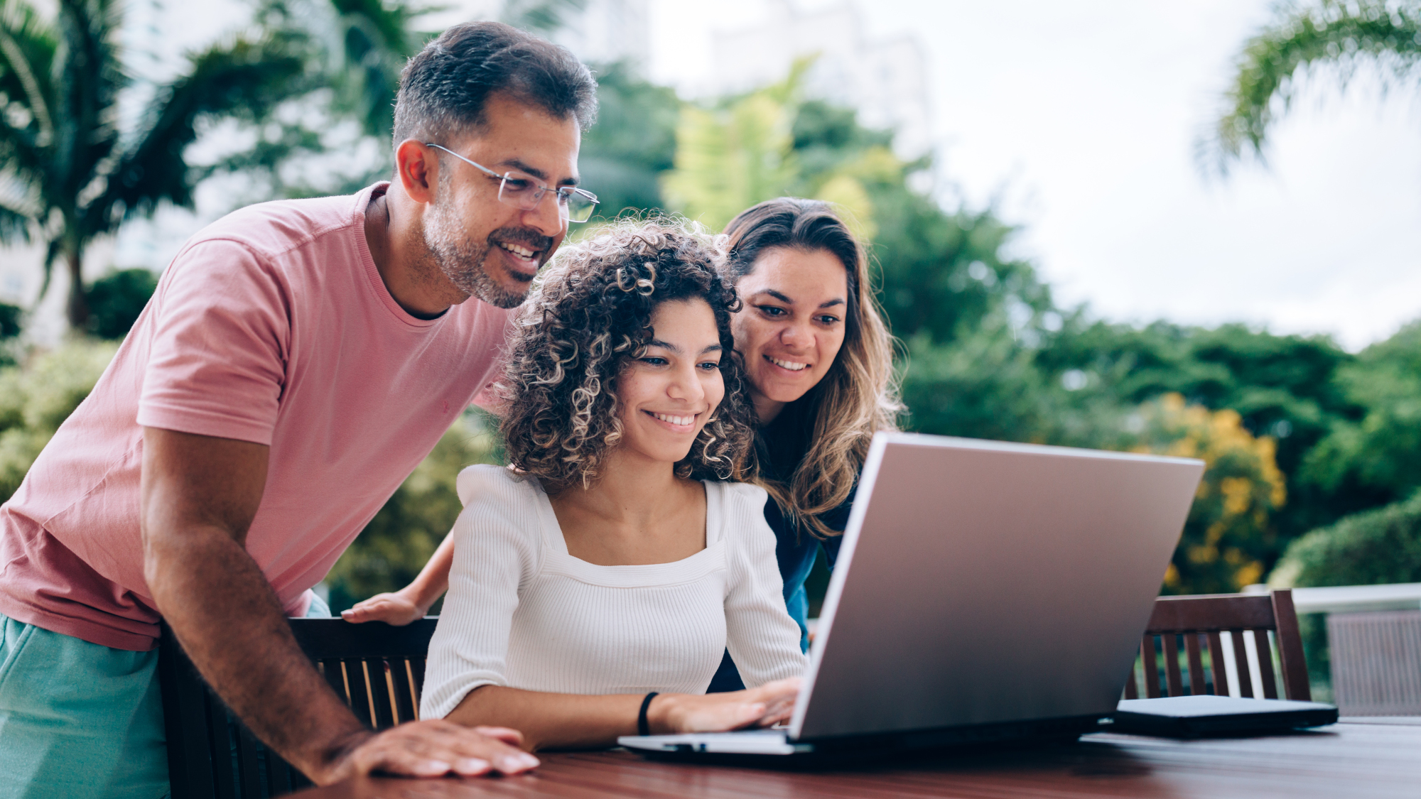 Family gathered around a laptop on a table outside in the garden