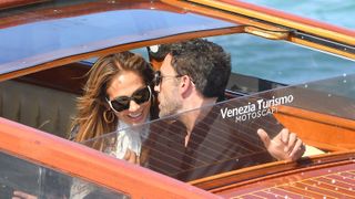 Jennifer Lopez smiles as Ben Affleck leans in to tell her something.