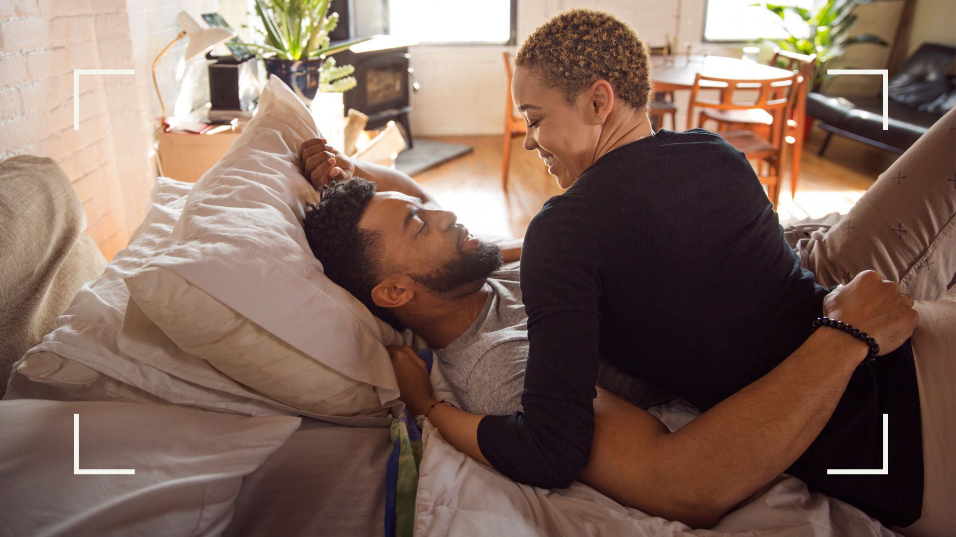 Couple lying in bed, laughing and smiling, about to try the full nelson sex position.