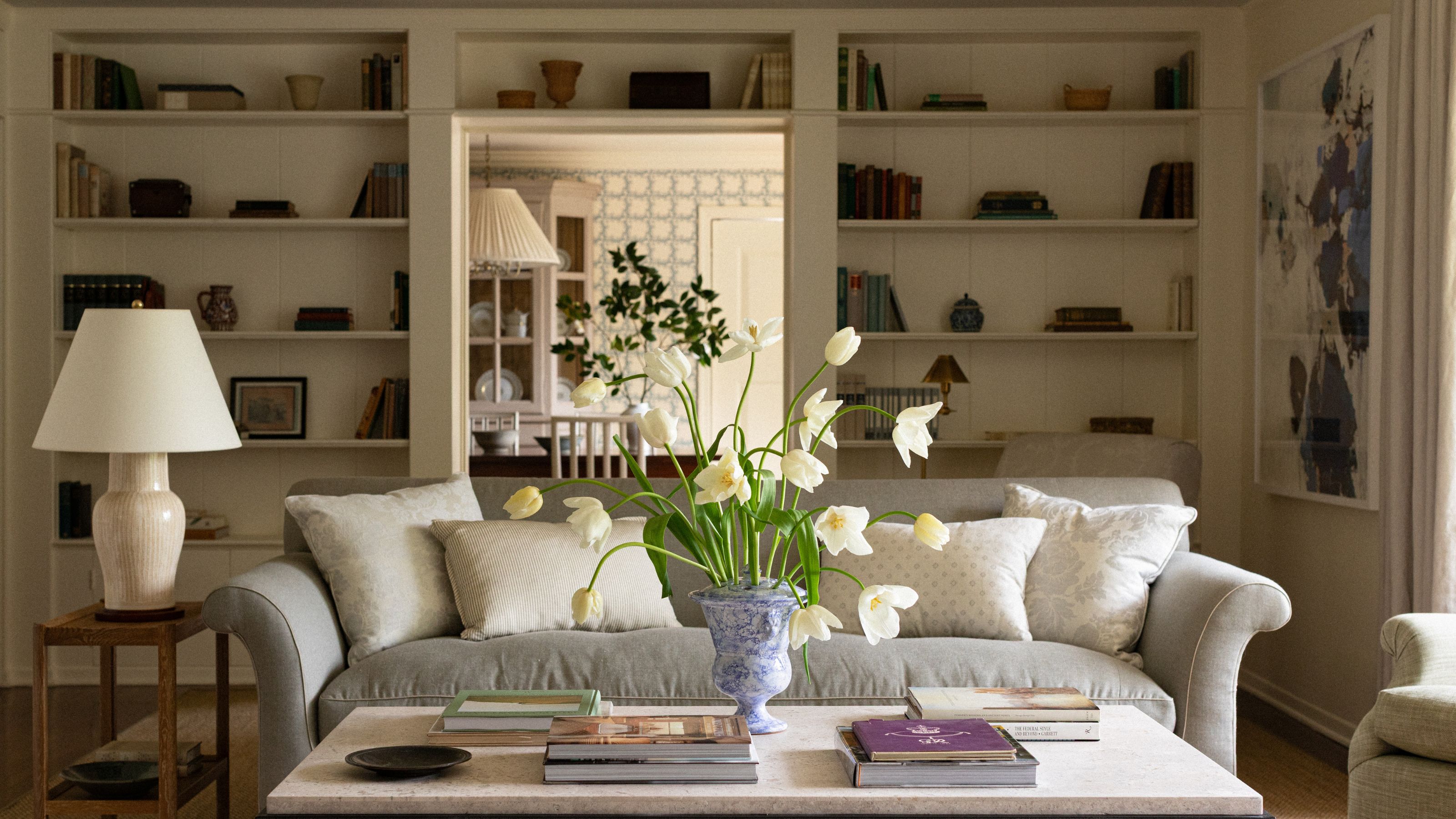 a warm neutral living room with a bookcase built around the doorway into the dining room