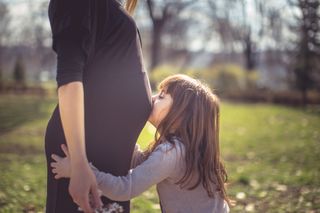 Little girl kissing her mother's pregnant stomach