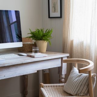 a home office with wooden desk and chair beside a window with an apple desktop computer