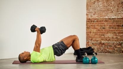 A man performing a glute bridge dumbbell floor press as part of a full-body dumbbell workout
