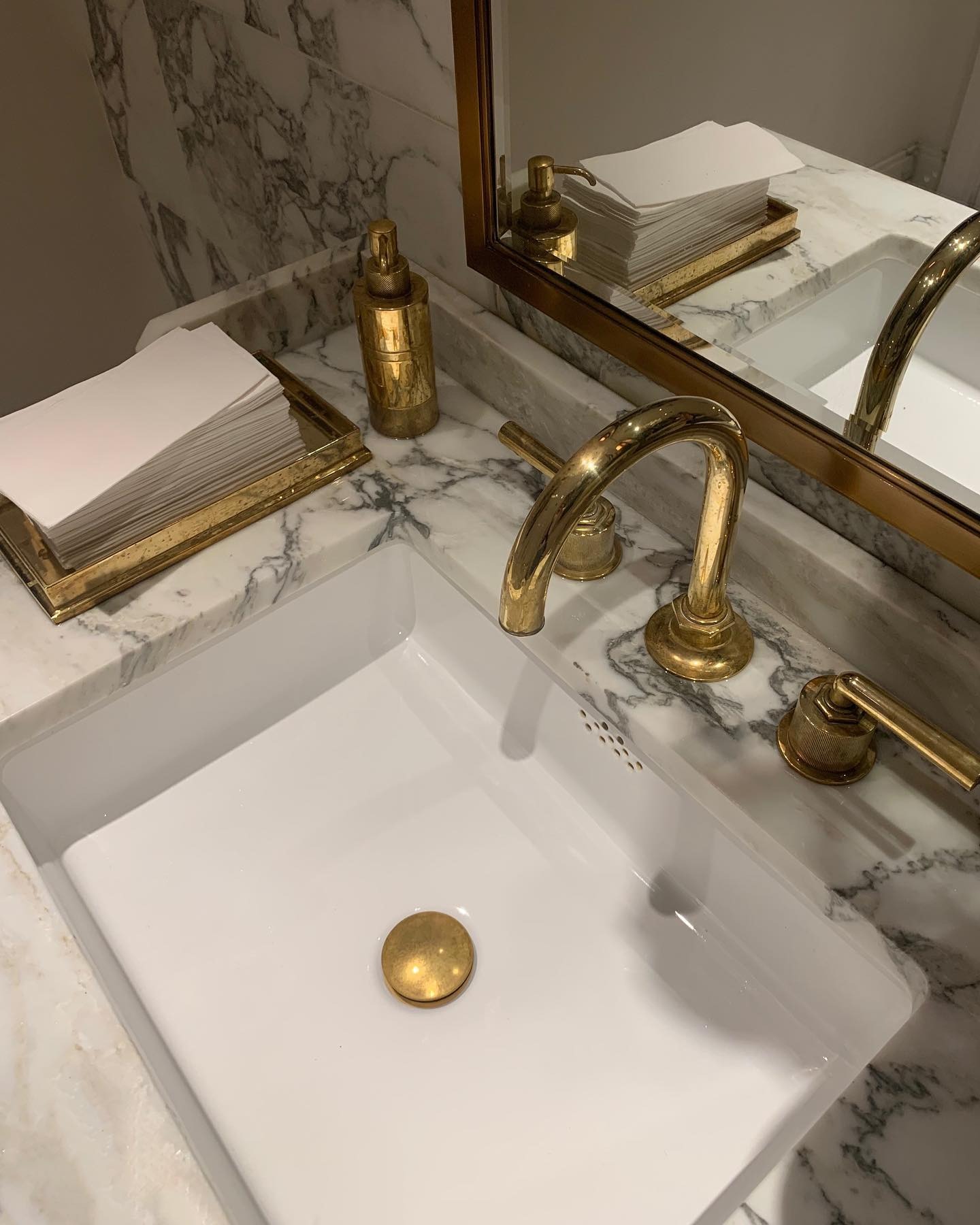 A grey and white marble sink with gold chrome faucet and taps