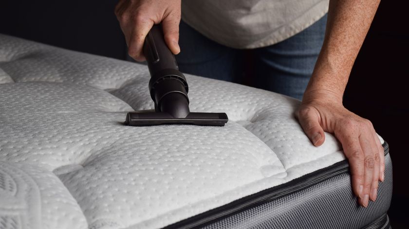 A person uses a handheld vacuum cleaner to vacuum a corner of a mattress