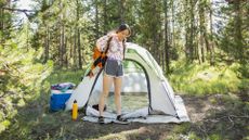 Young woman at campsite putting on backpack