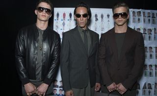 Three male models wearing clothing by Versace in dark shades.
