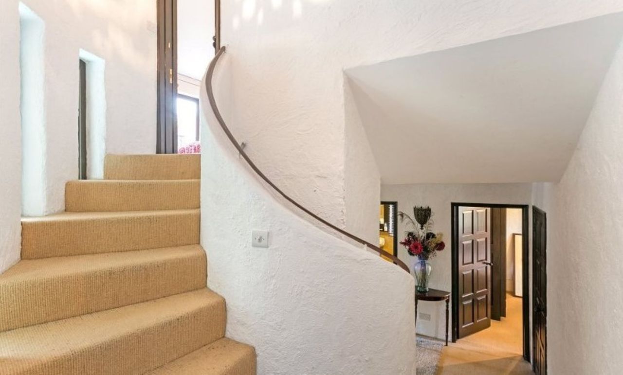 A curved staircase with orange carpet and white walls
