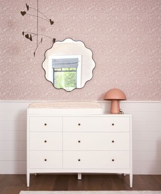 A white nursery dresser with a changing pad station and a pink mushroom lamp