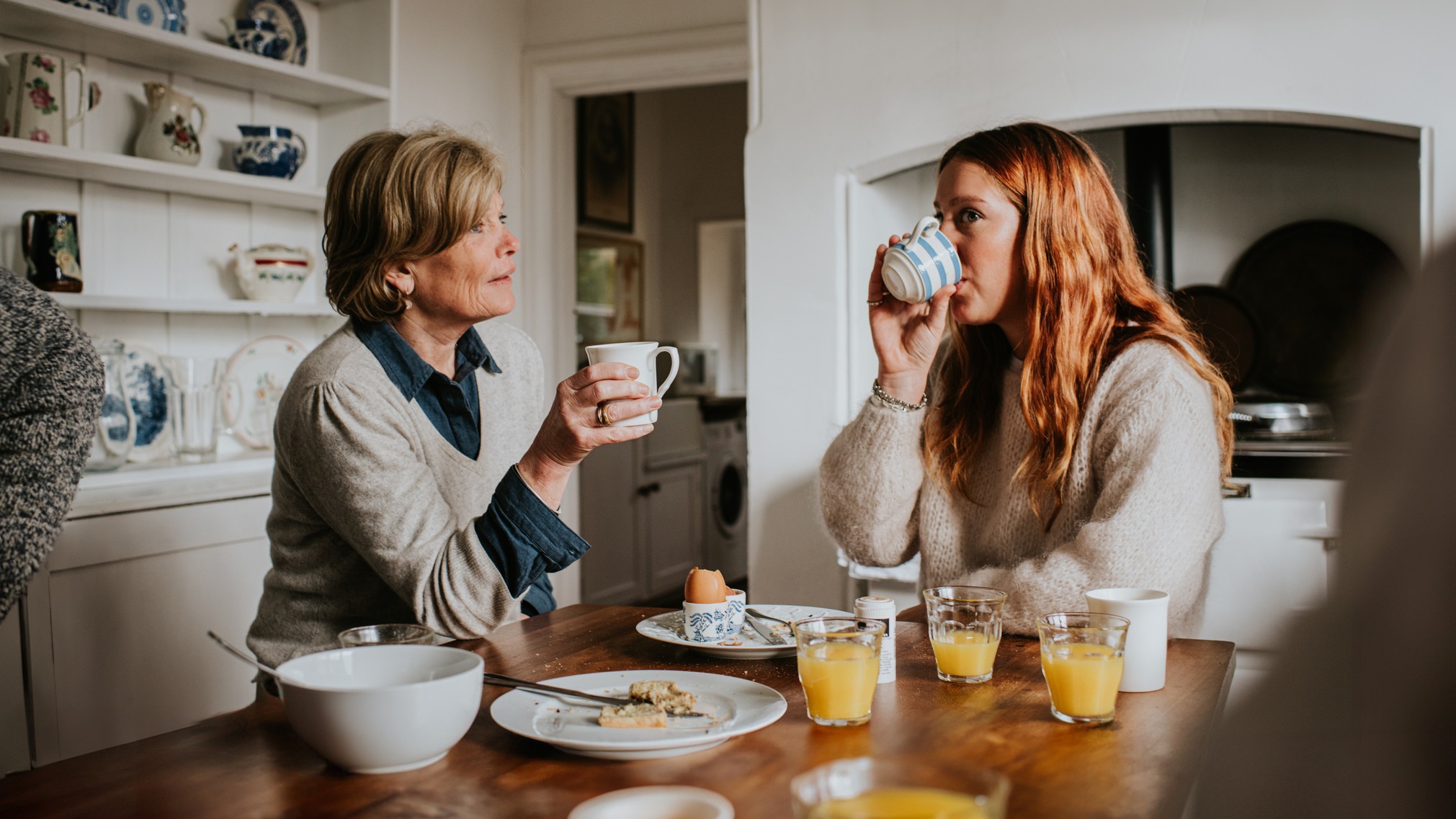 A woman sits at a table having breakfast with her mother. 