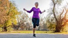 A woman jumps rope in a park. She is smiling and behind her we see trees and grass.