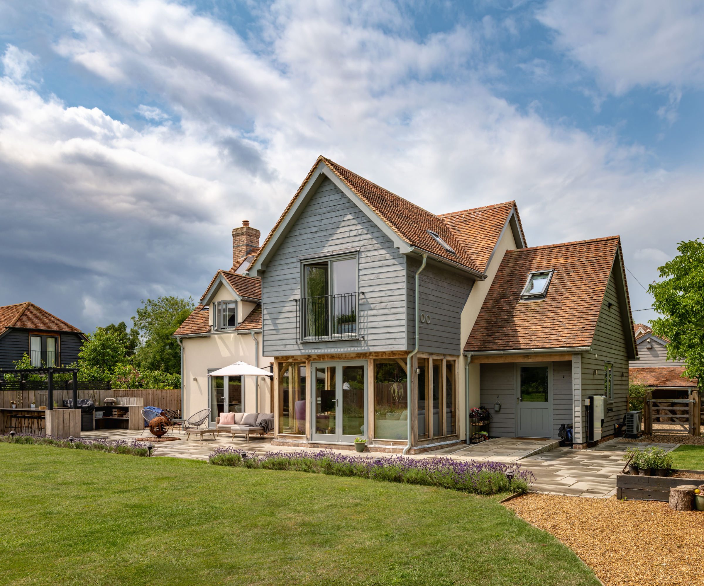 exterior shot of oak frame home with double storey extension to rear with green timber cladding, juliet balcony and large sections of glazing on ground floor