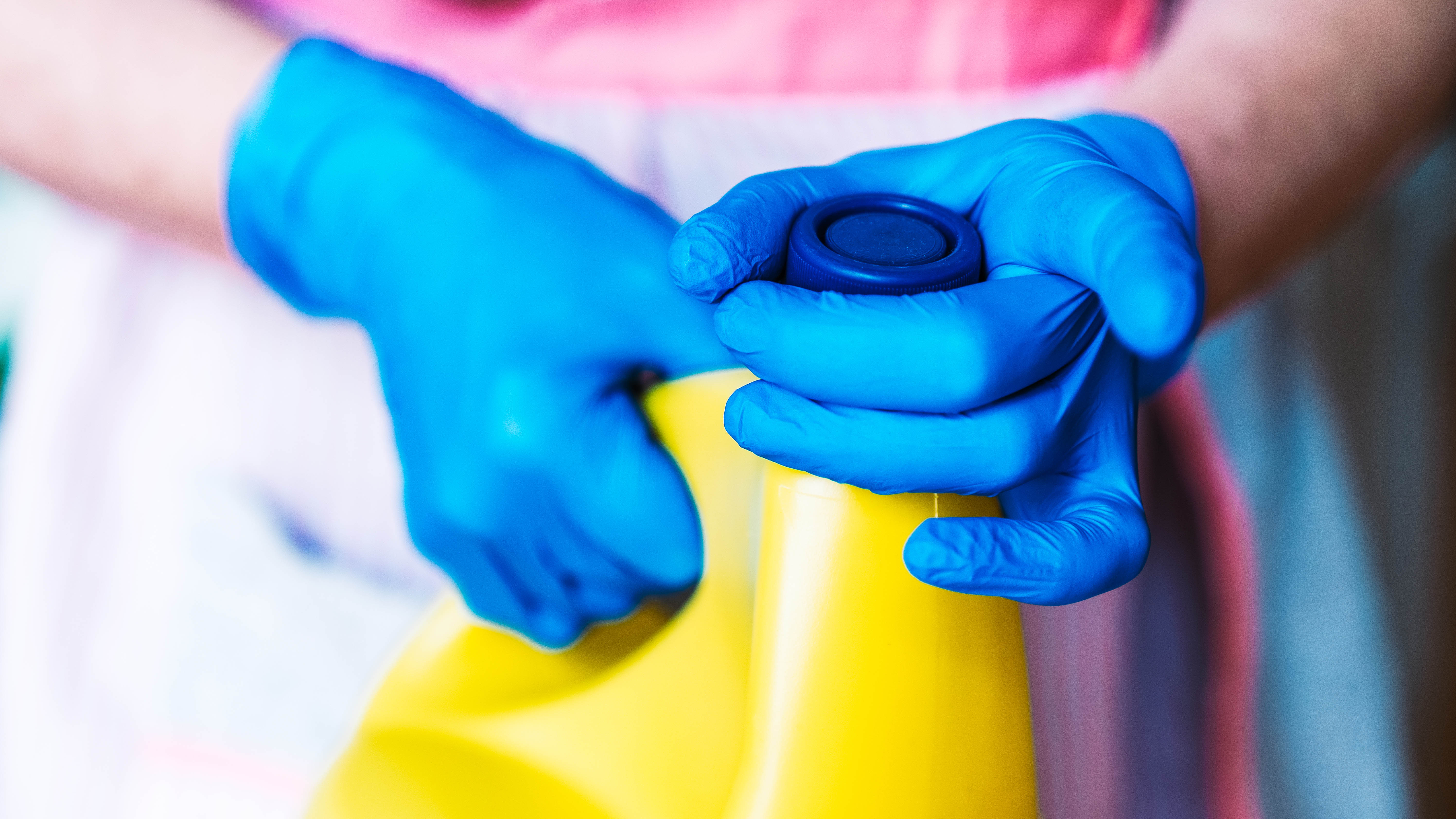 Someone wearing gloves removing the lid from a bottle of bleach