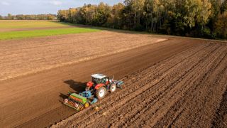 A red tractor pulling farm equipment across a large field