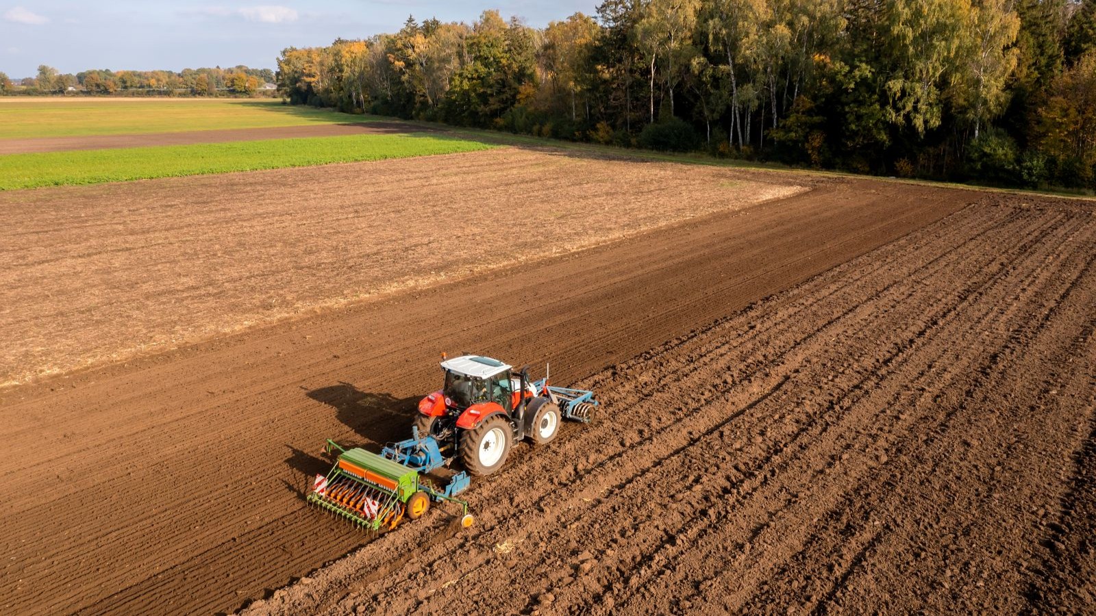 A red tractor pulling farm equipment across a large field