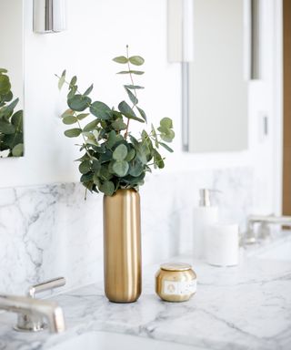 A gold vase filled with eucalyptus on a marble surface
