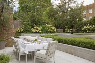 Outdoor patio furniture ideas featuring a long table laid with white linen in a town garden with white hydrangeas.
