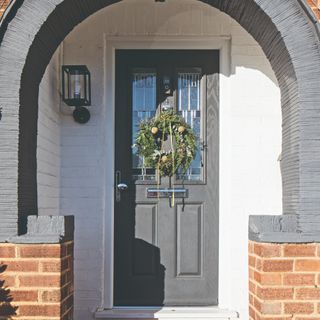 A grey front composite door surrounded by an arch and decorated with a Christmas wreath