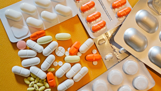 Collection of pills of different shapes, sizes and colors are shown against a yellow background. Next to them are pills that are still in their packets.