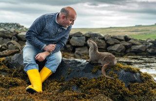 a person sat on a rock next to a locked looking at an otter who is sat next to them