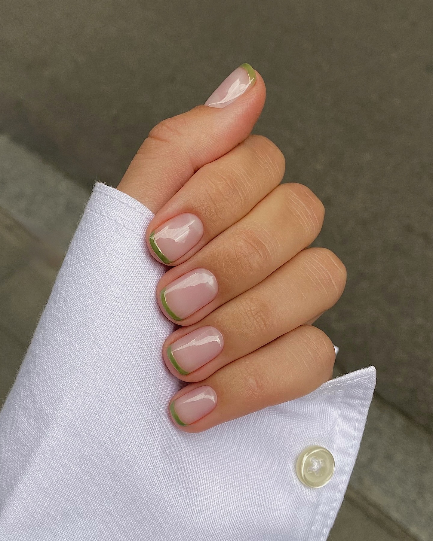 A close-up of a French manicure with olive green French tips