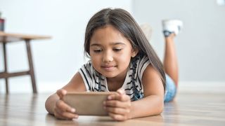 Smiling girl lies on floor looking at cell phone