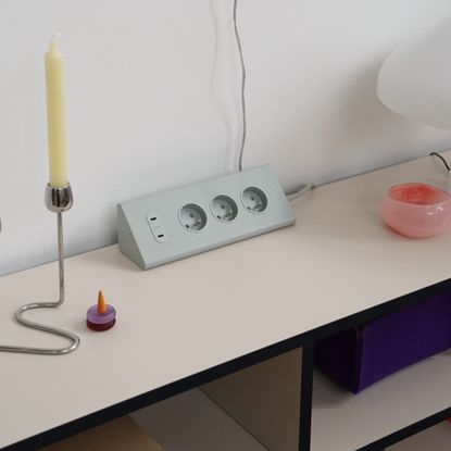 IKEA's SKOTAT extension cord on a sideboard with a chrome candlestick and a decorative glass bowl next to it