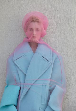 Photo of a person in a blue coat with thin pink fabric covering their face and coat