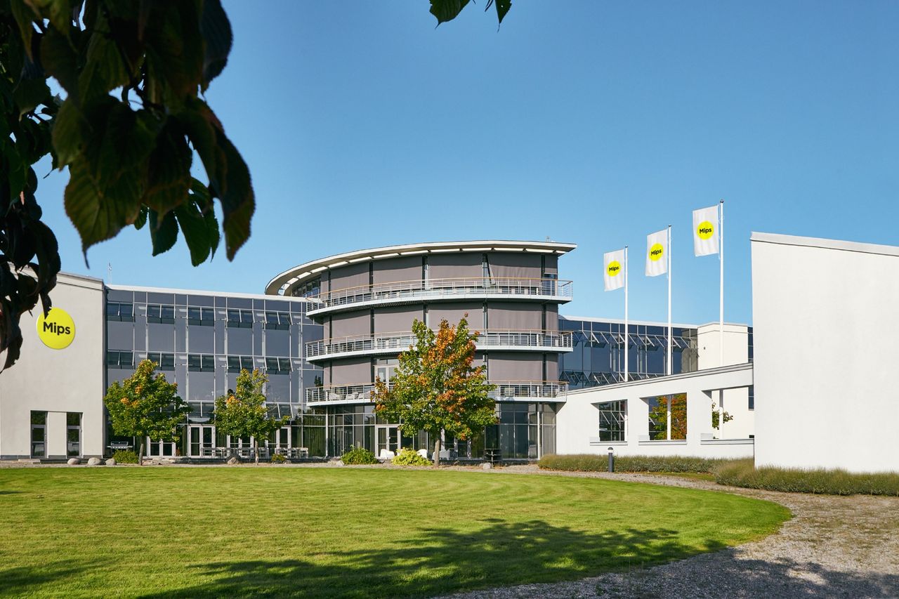 The MIPS HQ building shown with lawn at the front, flags to the right and blue sky