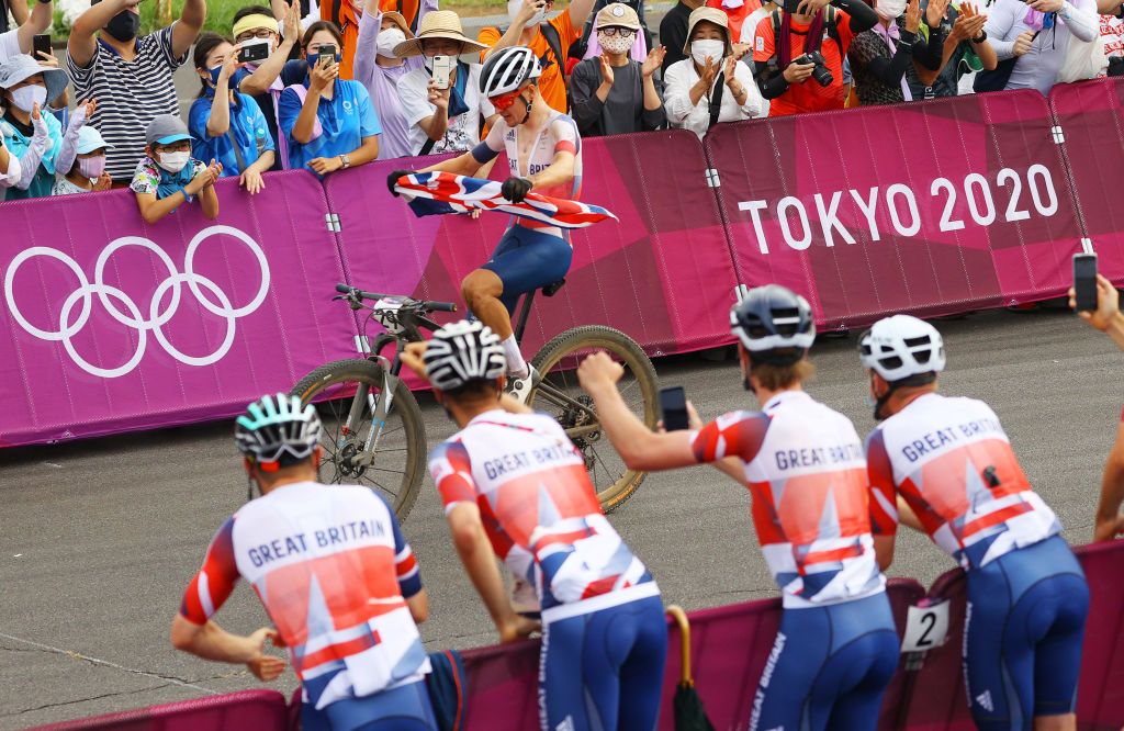 IZU JAPAN JULY 26 Thomas Pidcock of Team Great Britain celebrates winning the gold medal while holding the flag of his country encouraged by Team Great Britain during the Mens Crosscountry race on day three of the Tokyo 2020 Olympic Games at Izu Mountain Bike Course on July 26 2021 in Izu Shizuoka Japan Photo by Tim de WaeleGetty Images